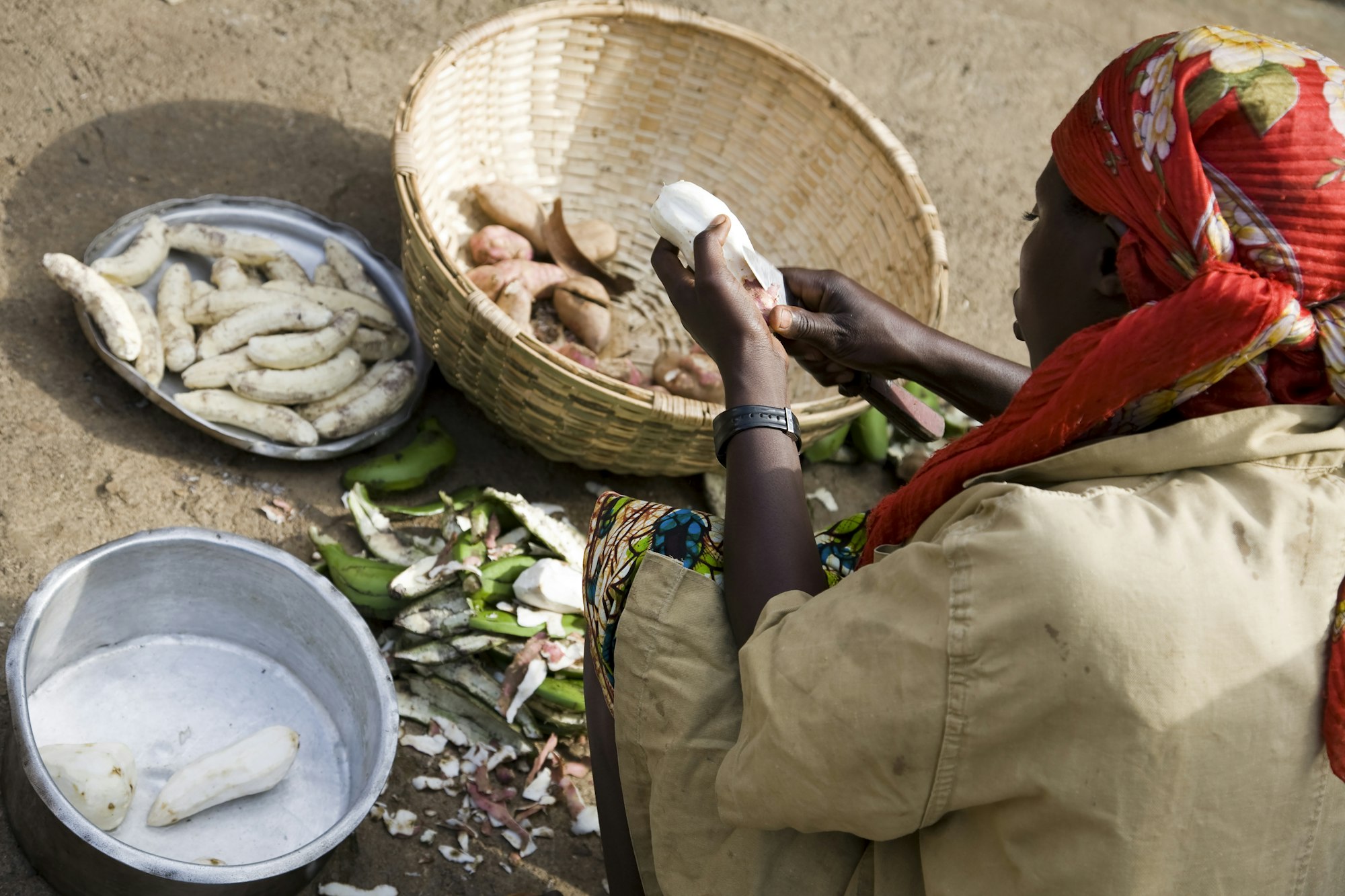 A woman meticulously peels cassava root in a traditional outdoor setting.